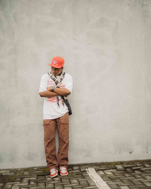Young man in fashionable casual wear with orange highlights against a textured urban wall.