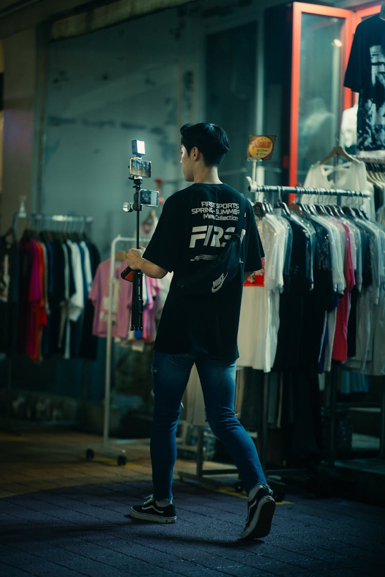 Young Man With Camera On Tripod Filming In Clothing Shop