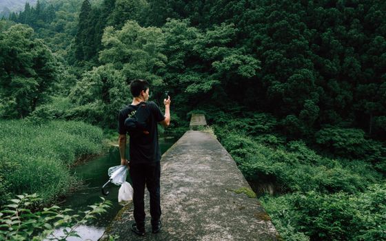 A man using a smartphone on a path in a verdant forest landscape.
