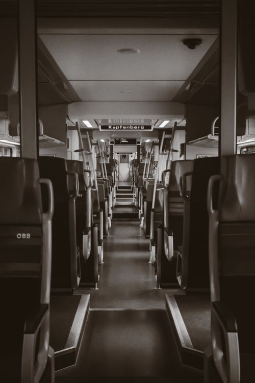Free A monochrome view inside a passenger train with a focus on the linear arrangement of seats and the Kapfenberg sign displayed. Stock Photo
