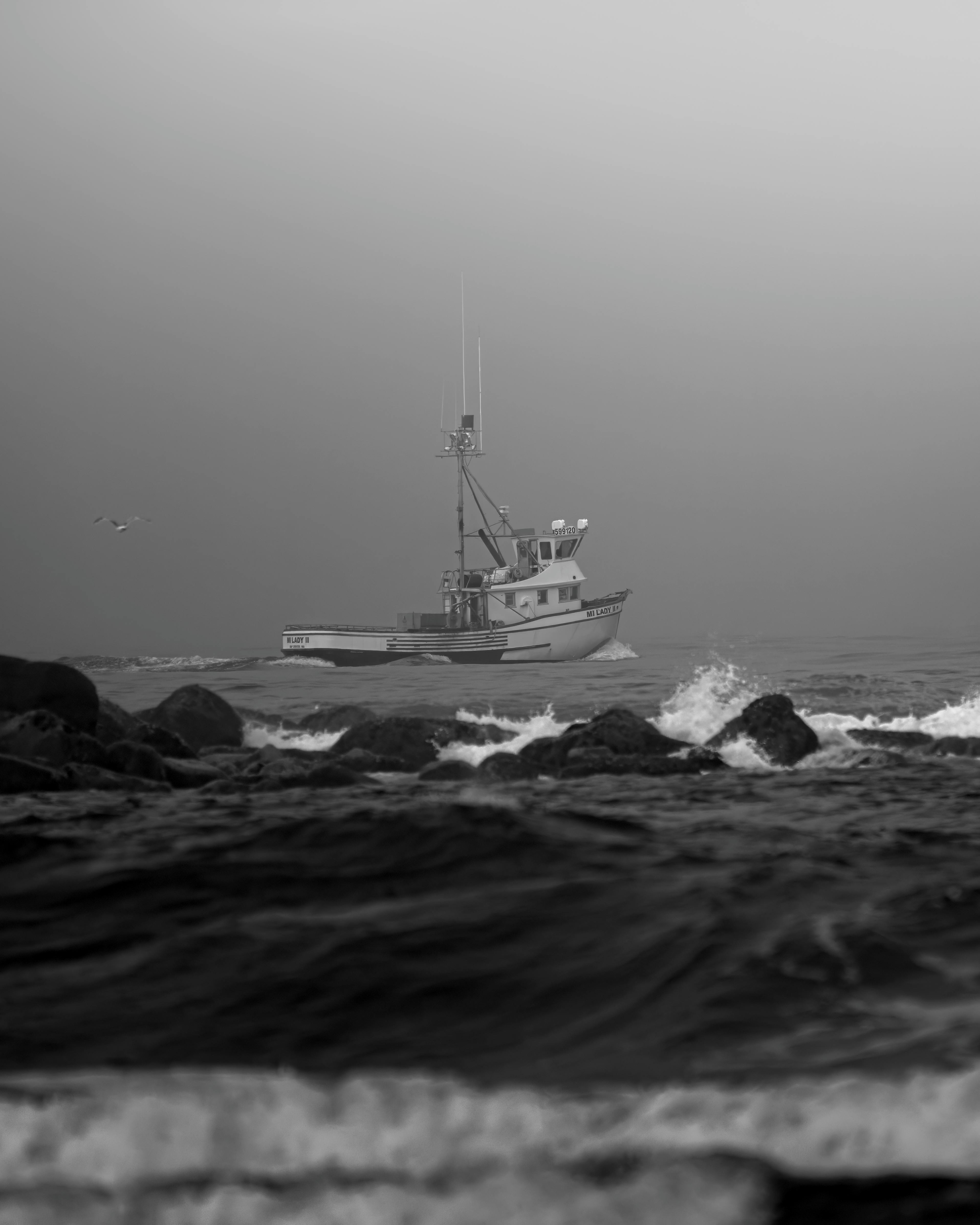 A fishing boat navigating the rocky shore of Ocean Shores in a monochrome theme.