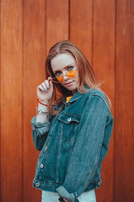 Young woman in denim jacket posing confidently with orange sunglasses in Mexico City.