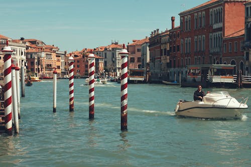 Man Sailing in a Motorboat past Striped Poles in Venice Grand Canal