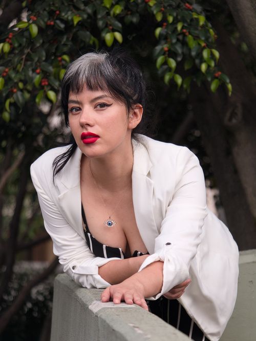 Free Captivating portrait of a woman in a white blazer leaning against a green railing outdoors. Stock Photo