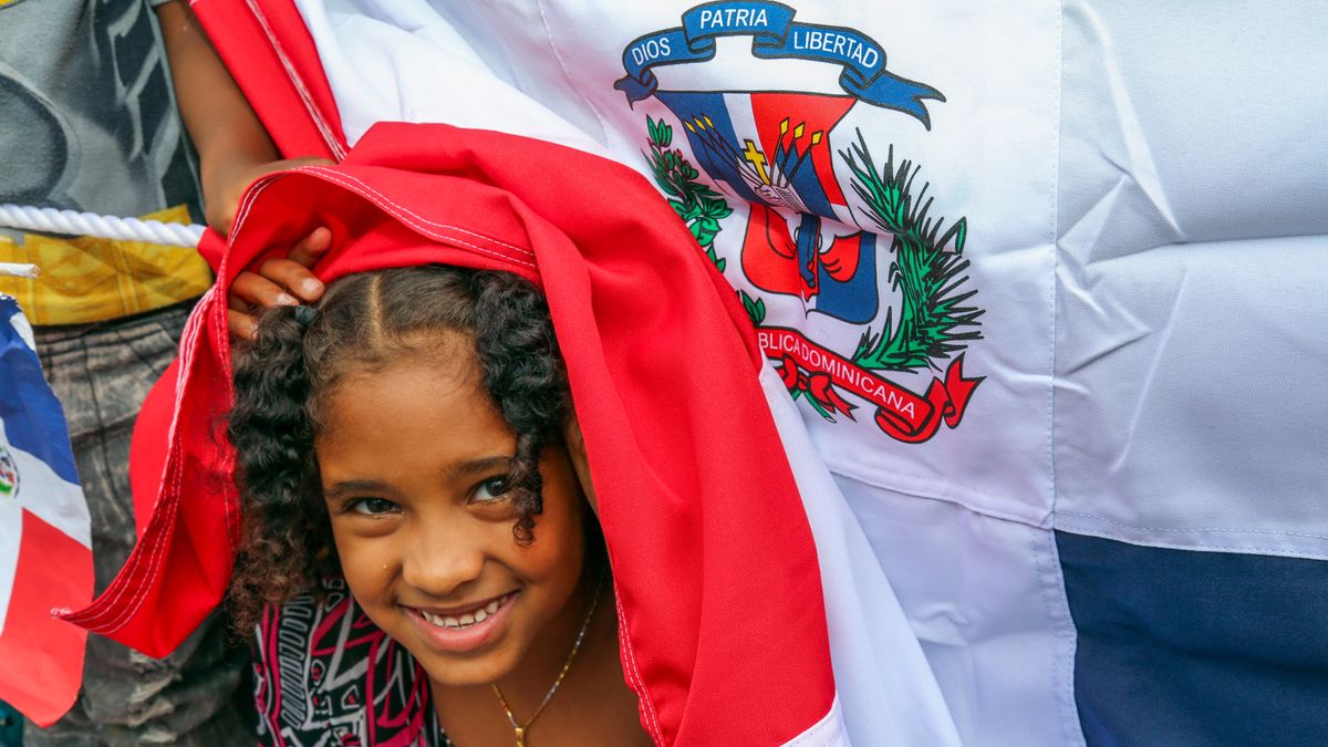 Cheerful young girl smiling beneath a Dominican Republic flag, celebrating natio