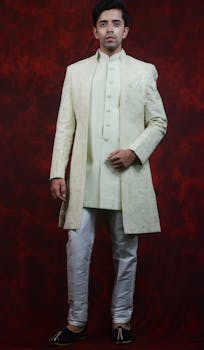 Elegant image of a man posing in a traditional sherwani outfit against a rich red backdrop.