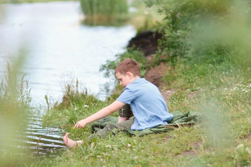Free Boy sitting by the riverside in summer, enjoying nature and relaxation. Stock Photo