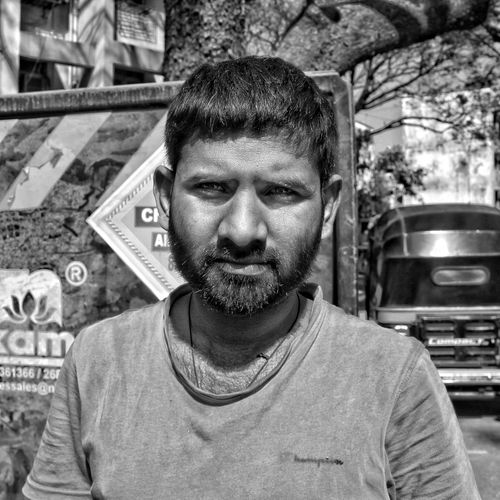 Free Black and white portrait of a bearded man standing outdoors in an urban setting. Stock Photo
