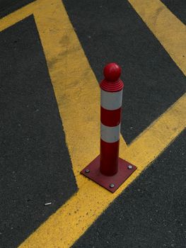 Vertical red bollard on asphalt with yellow striped lines, urban traffic safety.