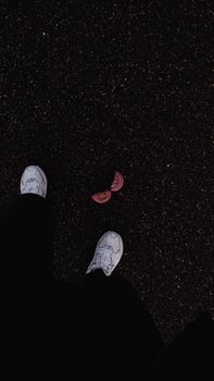 White shoes standing on textured asphalt with broken chewing gum in focus.