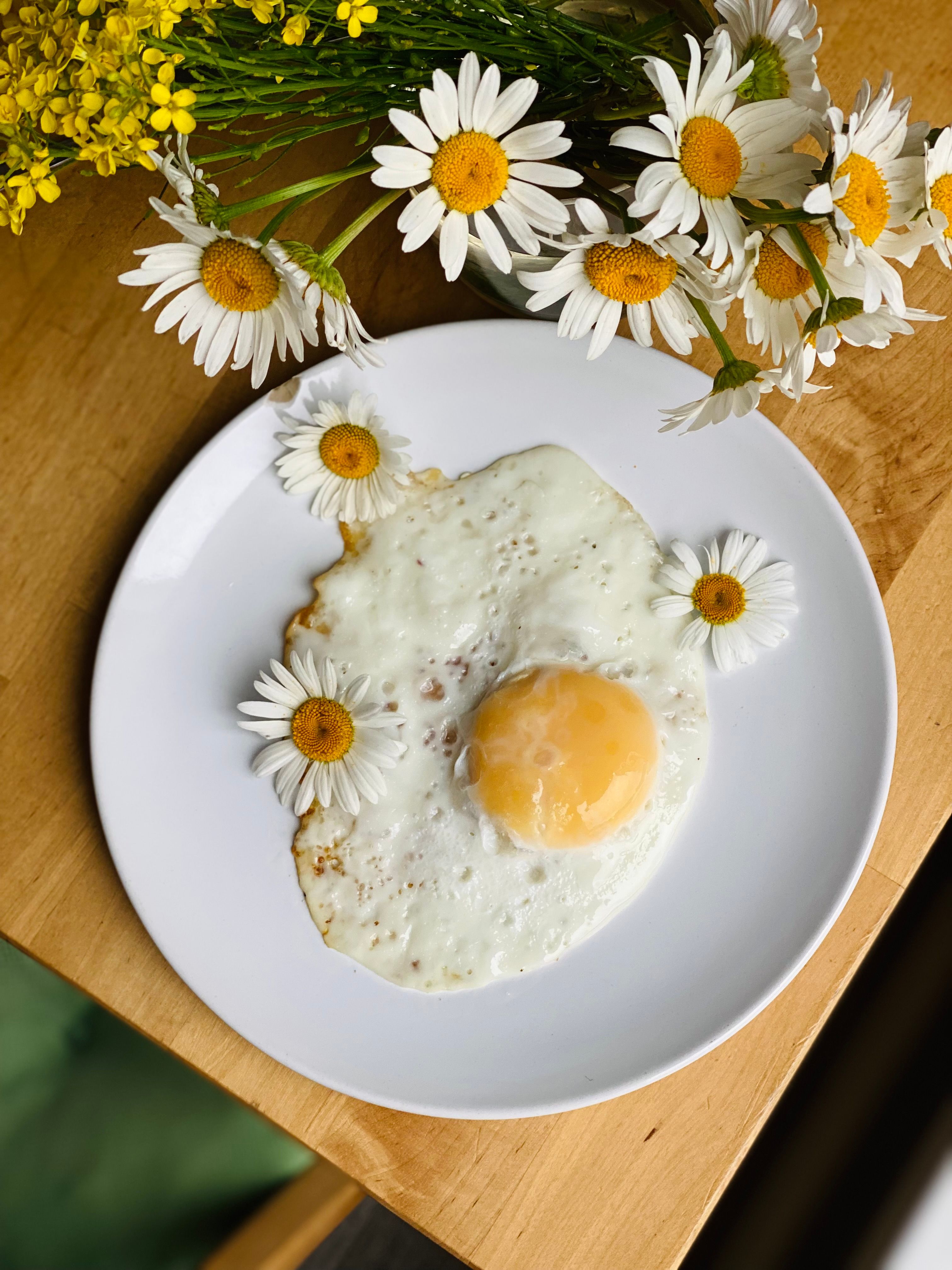 High-angle view of a fried egg adorned with chamomiles on a wooden table.
