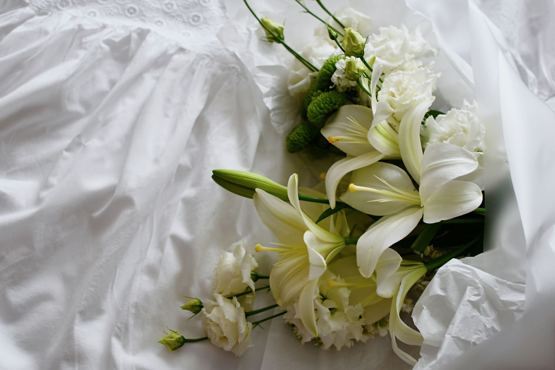 A bouquet of white lilies and carnations placed on delicate white fabric, perfect for wedding themes.