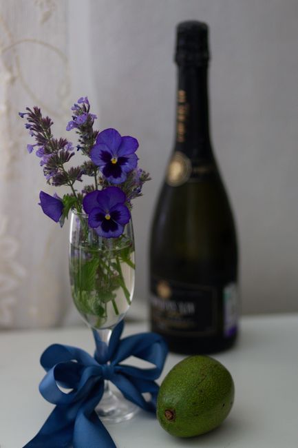 A sophisticated arrangement of a champagne bottle, flowers in a glass, and an avocado, perfect for celebrations.