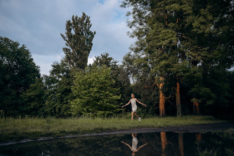 Teenager Girl In Summer Dress Running On Grass And Reflecting In A Rain Pool