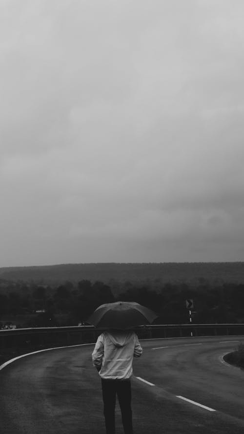 Man Standing in Rain on a Road Holding an Umbrella