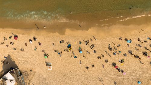 Free Drone aerial view of a sunlit beach with people lounging and playing by the shore in Rio de Janeiro. Stock Photo