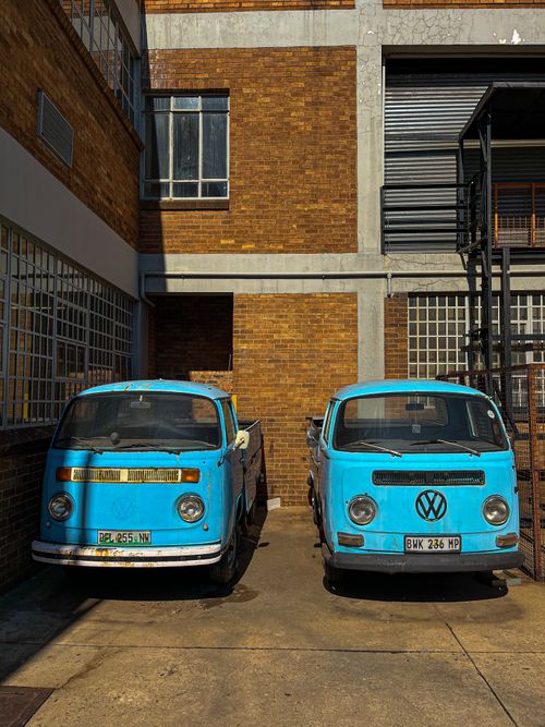 Free Two vintage blue Volkswagen vans parked beside an old brick building in Johannesburg, South Africa. Stock Photo