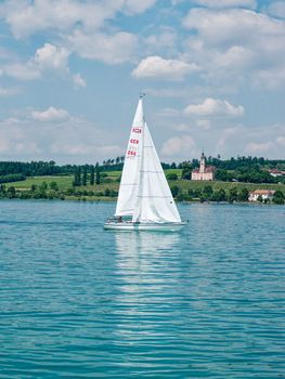 A peaceful sailboat on Bodensee with Birnau Church in the background under a summer sky.