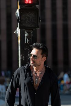 Fashionable man with sunglasses and tattoos poses at a city crosswalk during the day.
