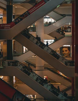 Interior view of a bustling shopping mall with multiple escalators and shoppers.