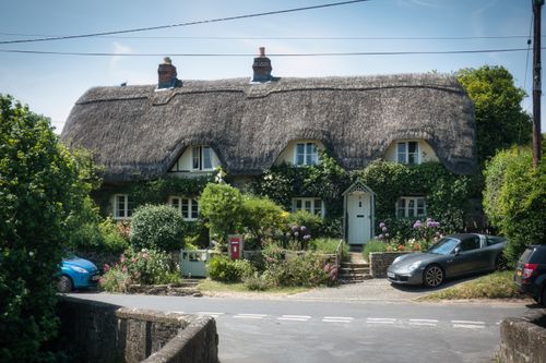 Free Picturesque thatched cottage with lush garden and a convertible car parked outside. Stock Photo