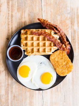 Tasty breakfast composed of eggs, waffles, and crispy bacon on rustic wooden table.