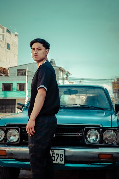 Free A young man stands casually in front of a retro vintage Datsun car on a sunny day outdoors. Stock Photo