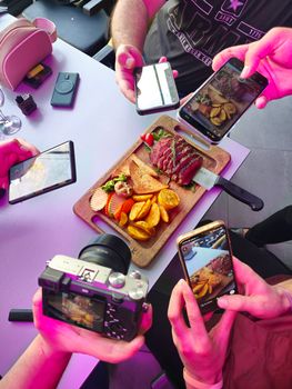 Group taking vibrant photos of gourmet meal with smartphones and camera.