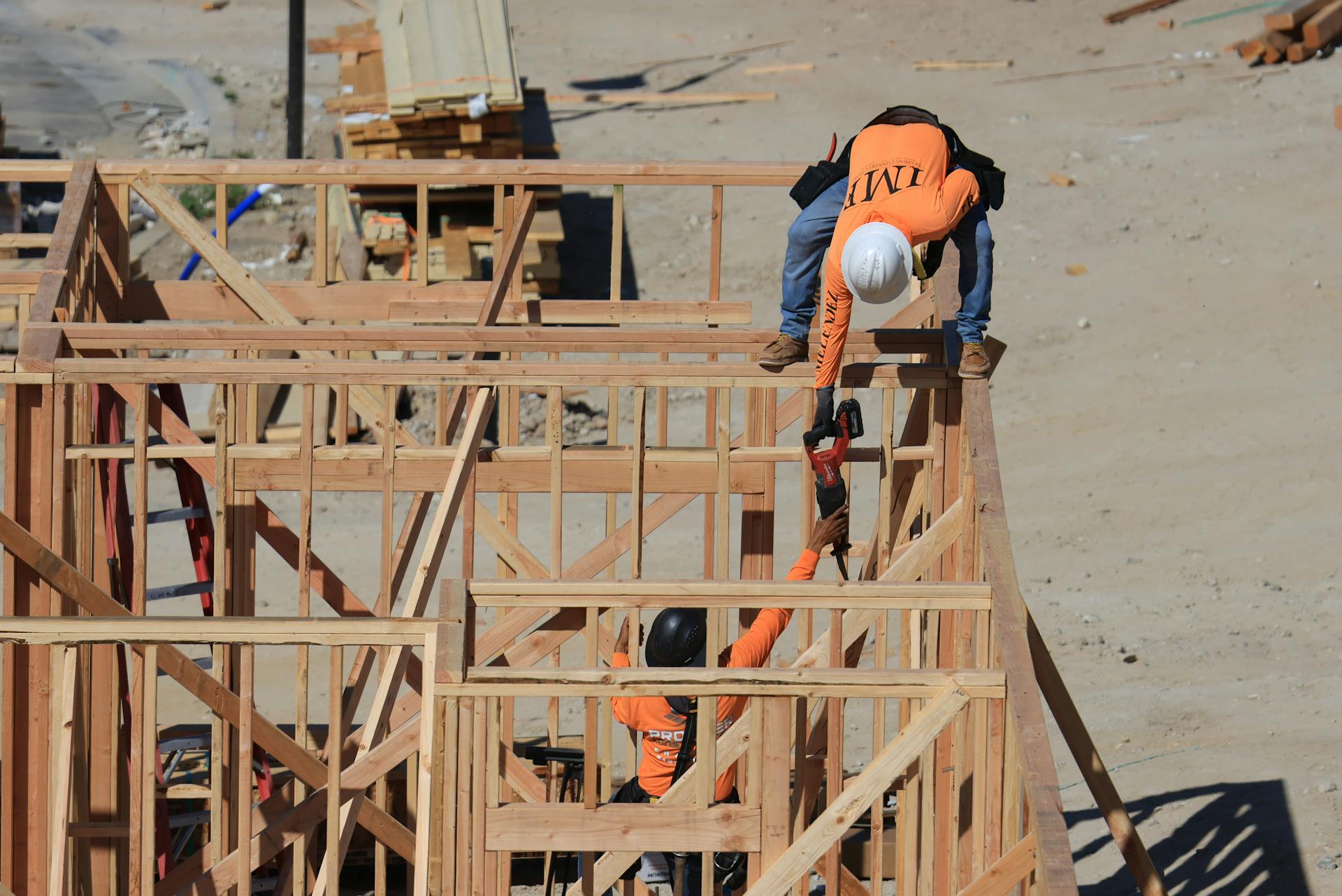 Two construction workers framing a wooden structure outdoors at a building site.