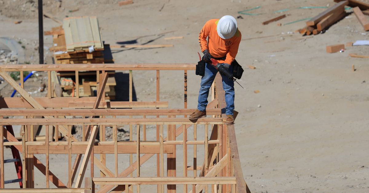 Photo by David Brown A construction worker wearing a safety helmet uses a drill on a wooden framework at a construction site.