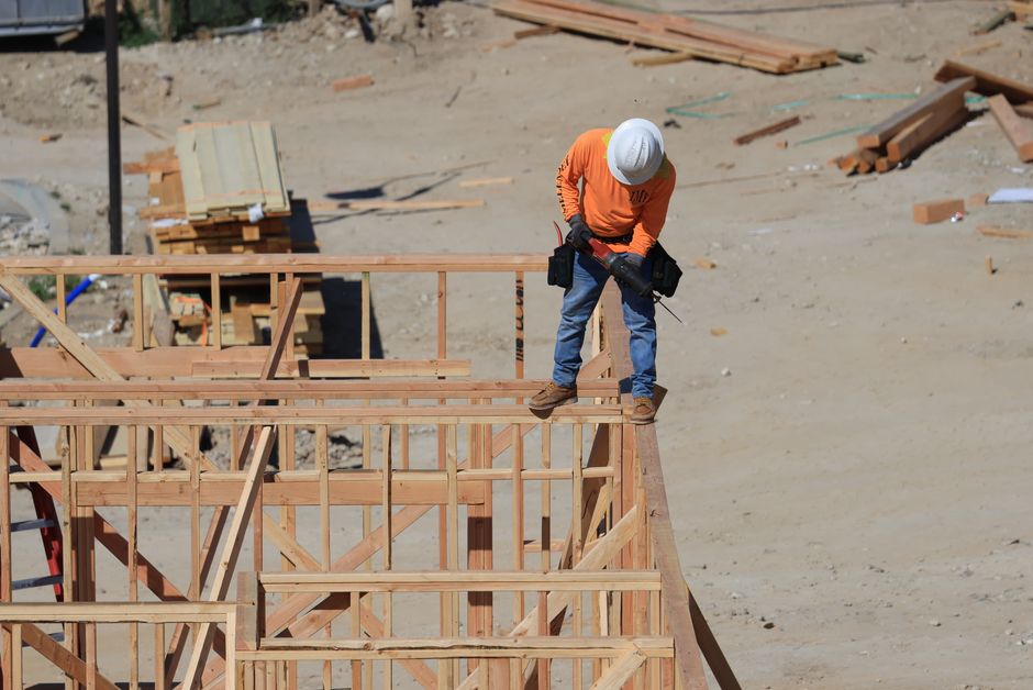 Photo by David Brown A construction worker wearing a safety helmet uses a drill on a wooden framework at a construction site.