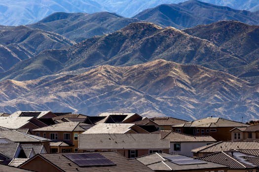 Residential area with houses and solar panels set against scenic mountains.