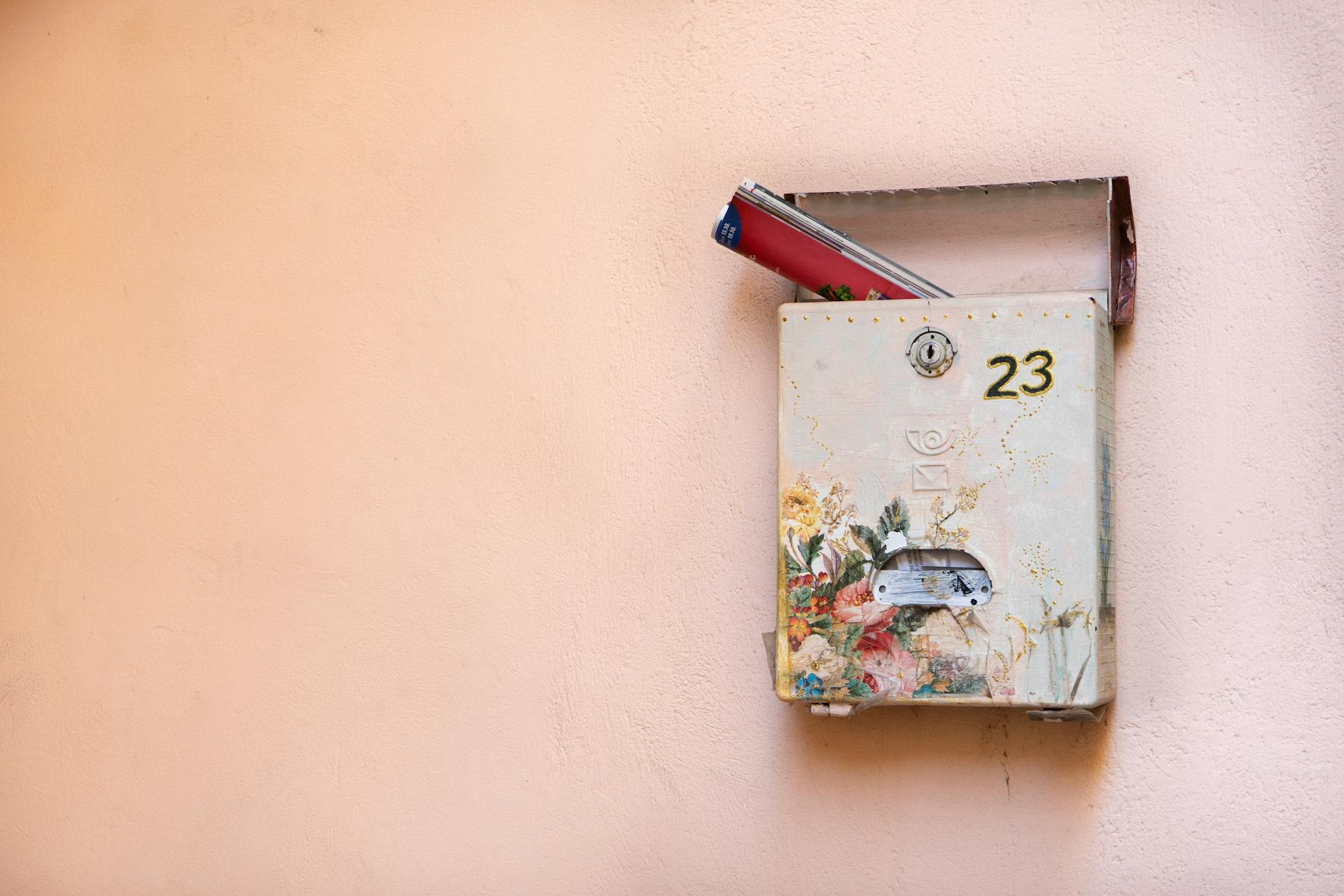 A decorative mailbox on a wall containing magazines, marked with number 23.