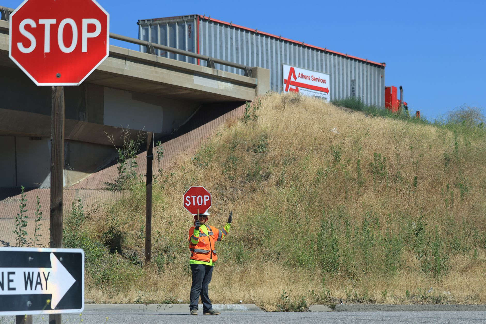 Construction worker with stop sign managing traffic near a bridge.