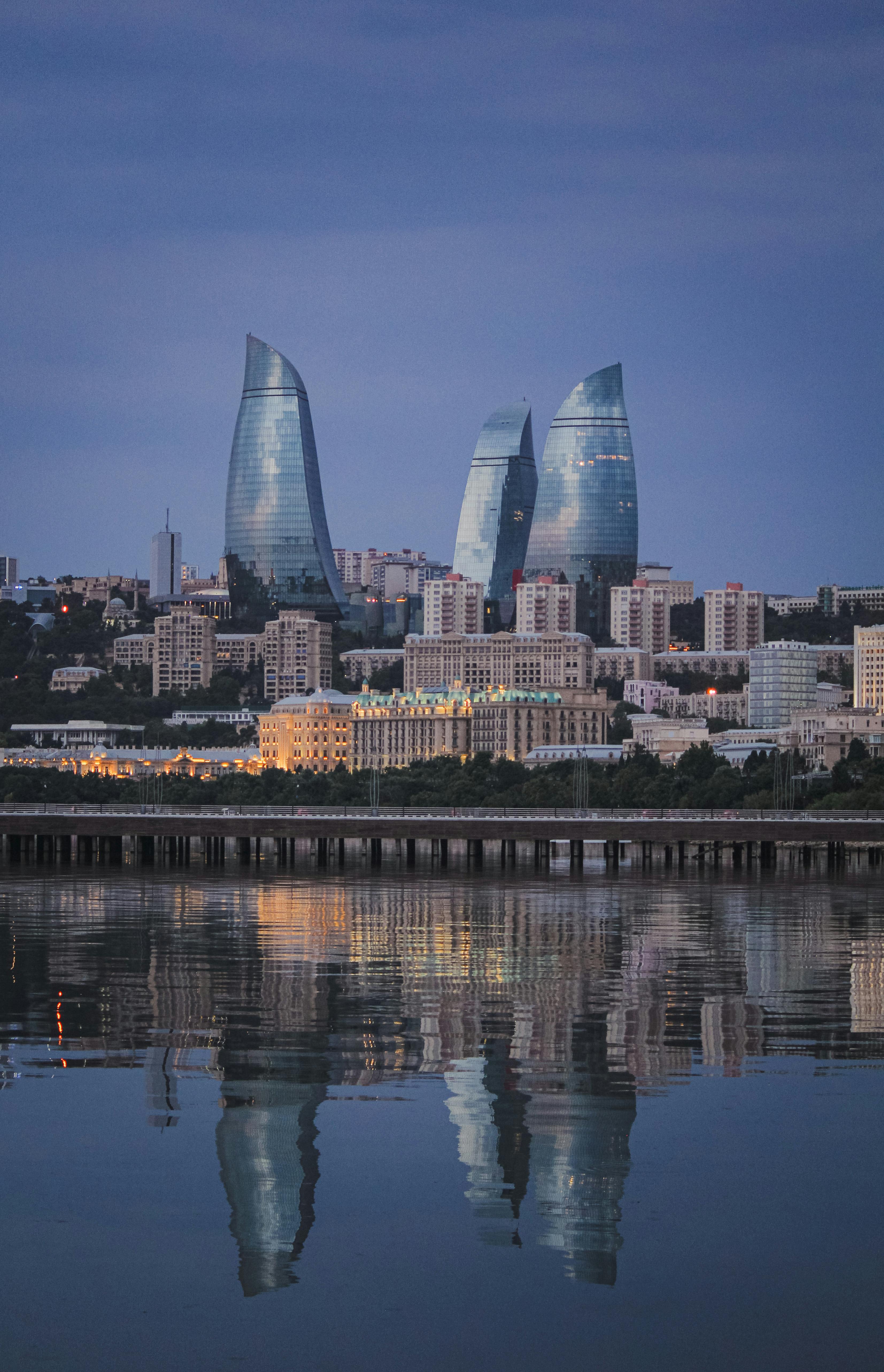 Capture of Baku's iconic Flame Towers reflected in the sea at dusk, showcasing modern architecture.