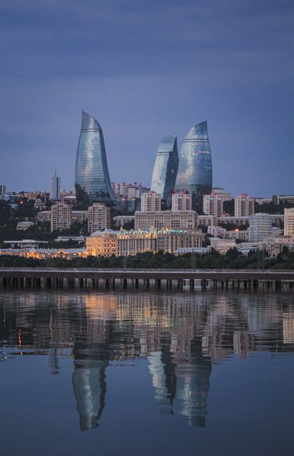 Capture of Baku's iconic Flame Towers reflected in the sea at dusk, showcasing modern architecture.