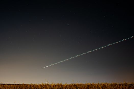 A serene night sky over the countryside with a light trail and distant stars in Madrid, Spain.