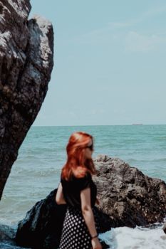 Red-haired woman enjoys coastal rocks with sea view.