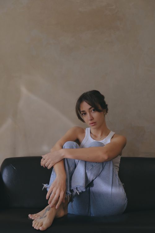 Free A relaxed woman in casual attire seated on a black sofa indoors. Stock Photo