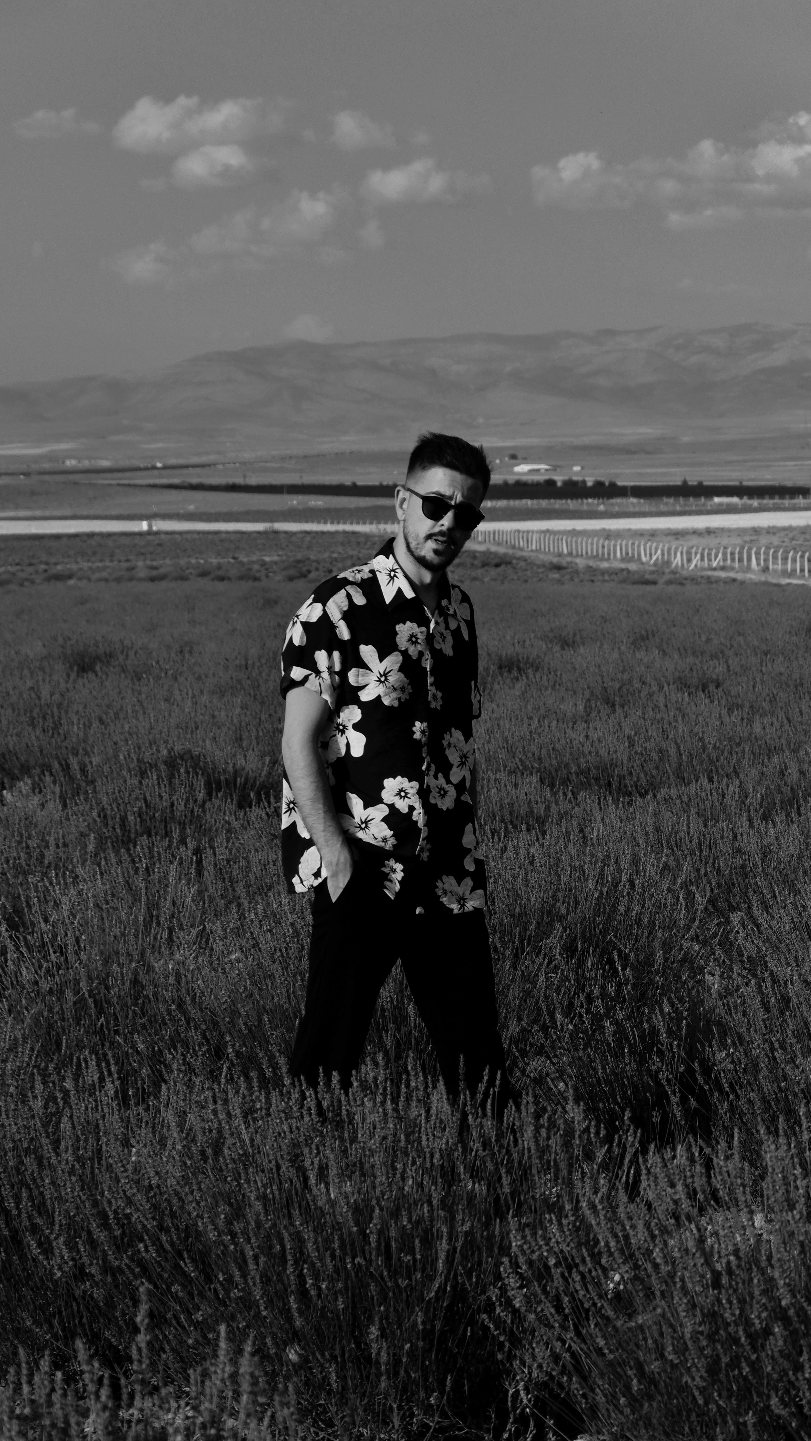 Young man in a floral shirt enjoying a summer day in a lavender field with sunglasses.