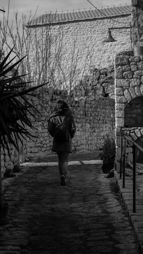 Back View of a Woman Walking between Stone Walls 