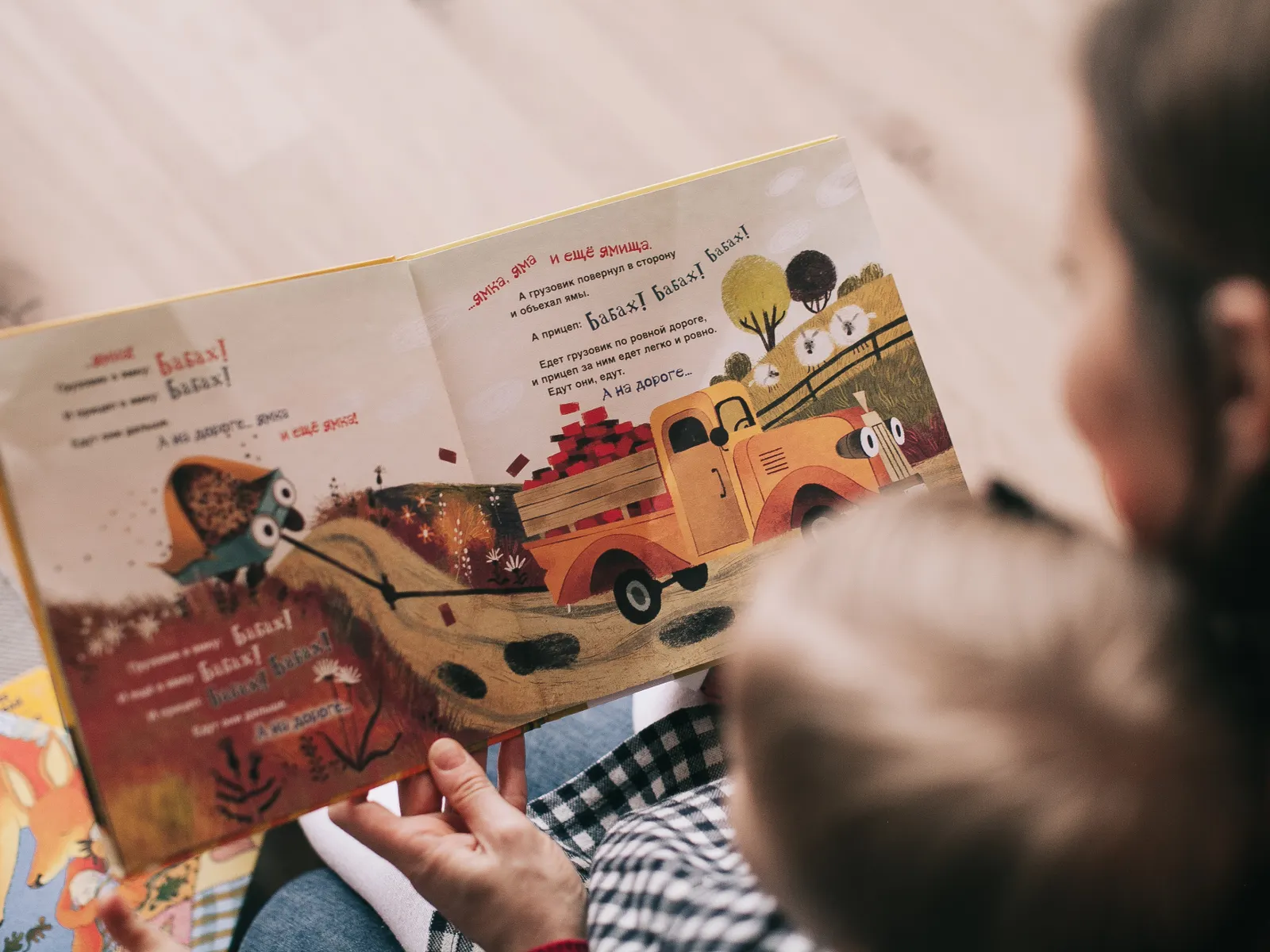 A mother and toddler sitting together indoors, sharing an illustrated picture book