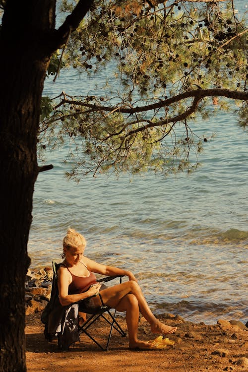 Free A Woman Sitting on a Folding Chair on the Beach  Stock Photo