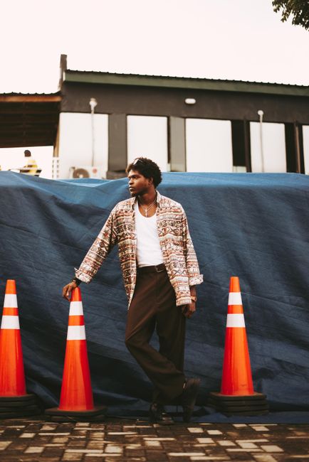 Stylish man poses in urban setting with bright traffic cones.