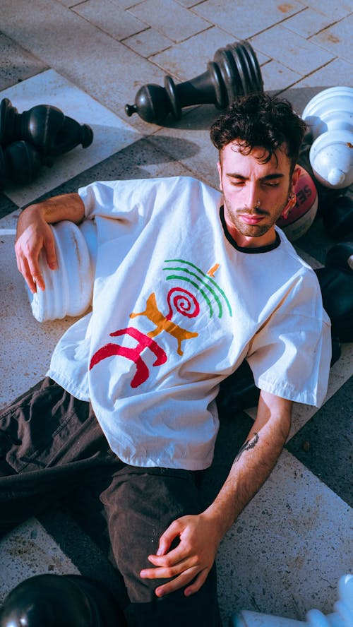 Man Lying Down on Pavement in White T-shirt