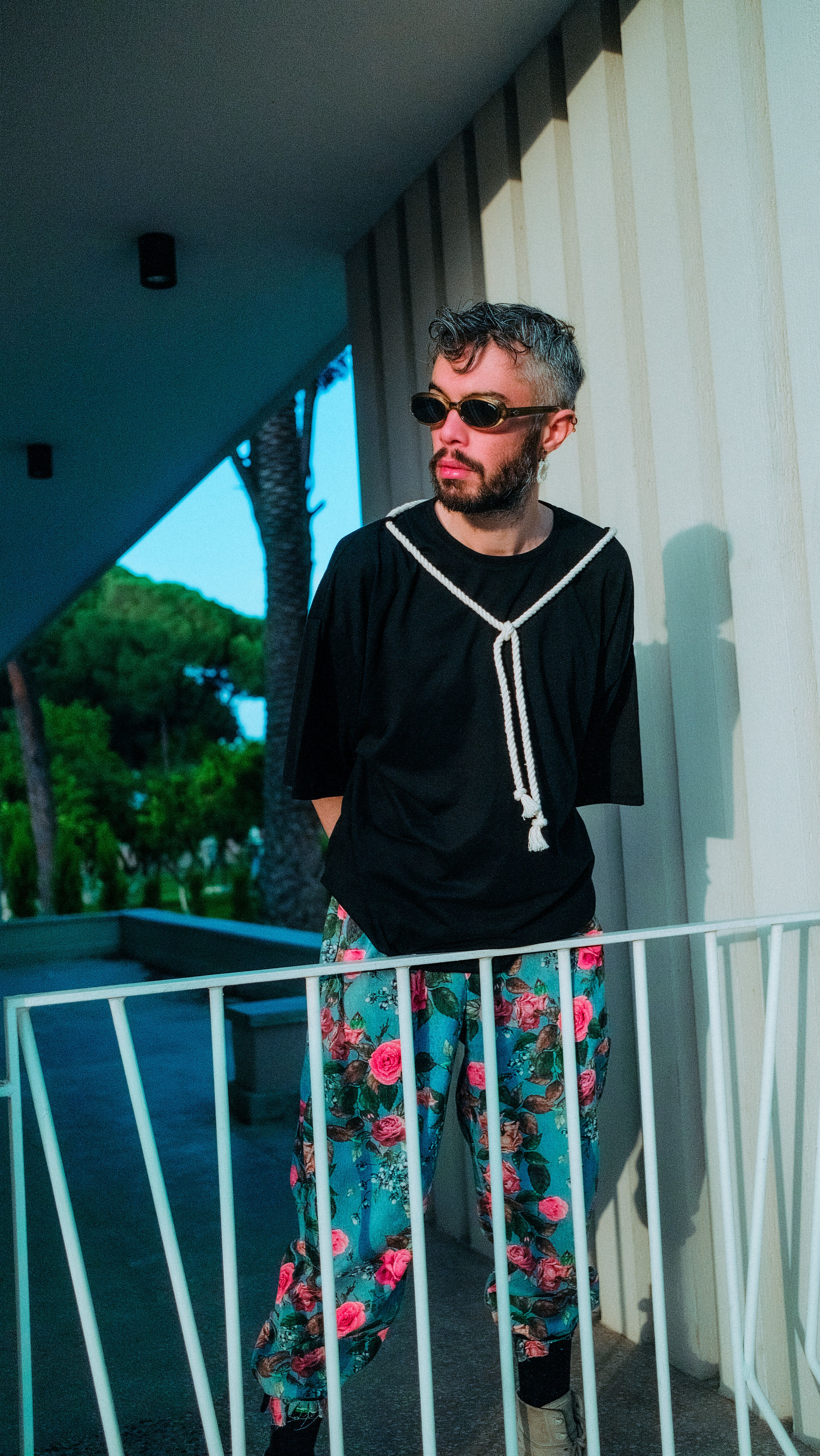 Fashionable man in sunglasses posing outside in floral pants and black t-shirt.