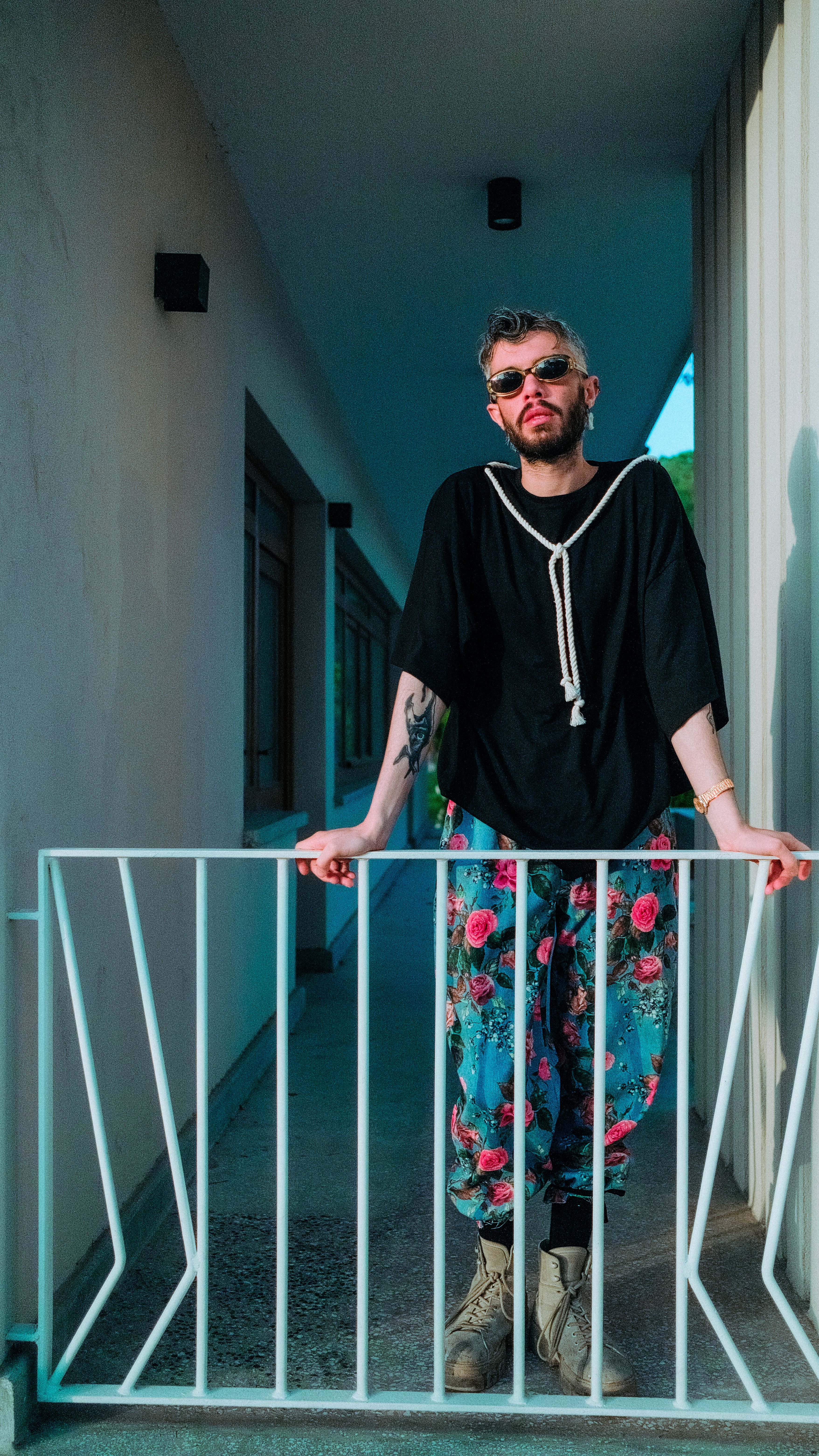 Fashionable man wearing floral pants and sunglasses leaning on a railing. Stylish urban vibe.