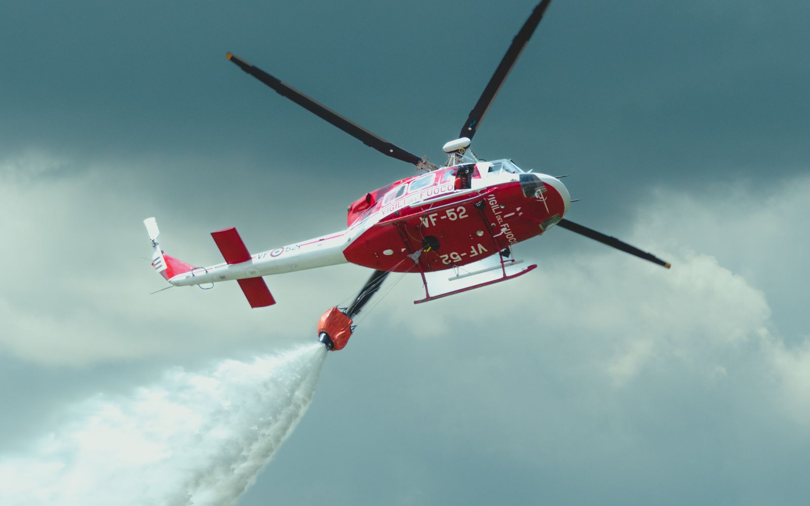 A firefighting helicopter releasing water over a forested hillside.