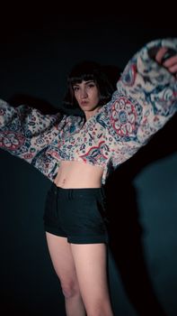 Caucasian woman in a floral blouse and shorts posing confidently in a studio setting.