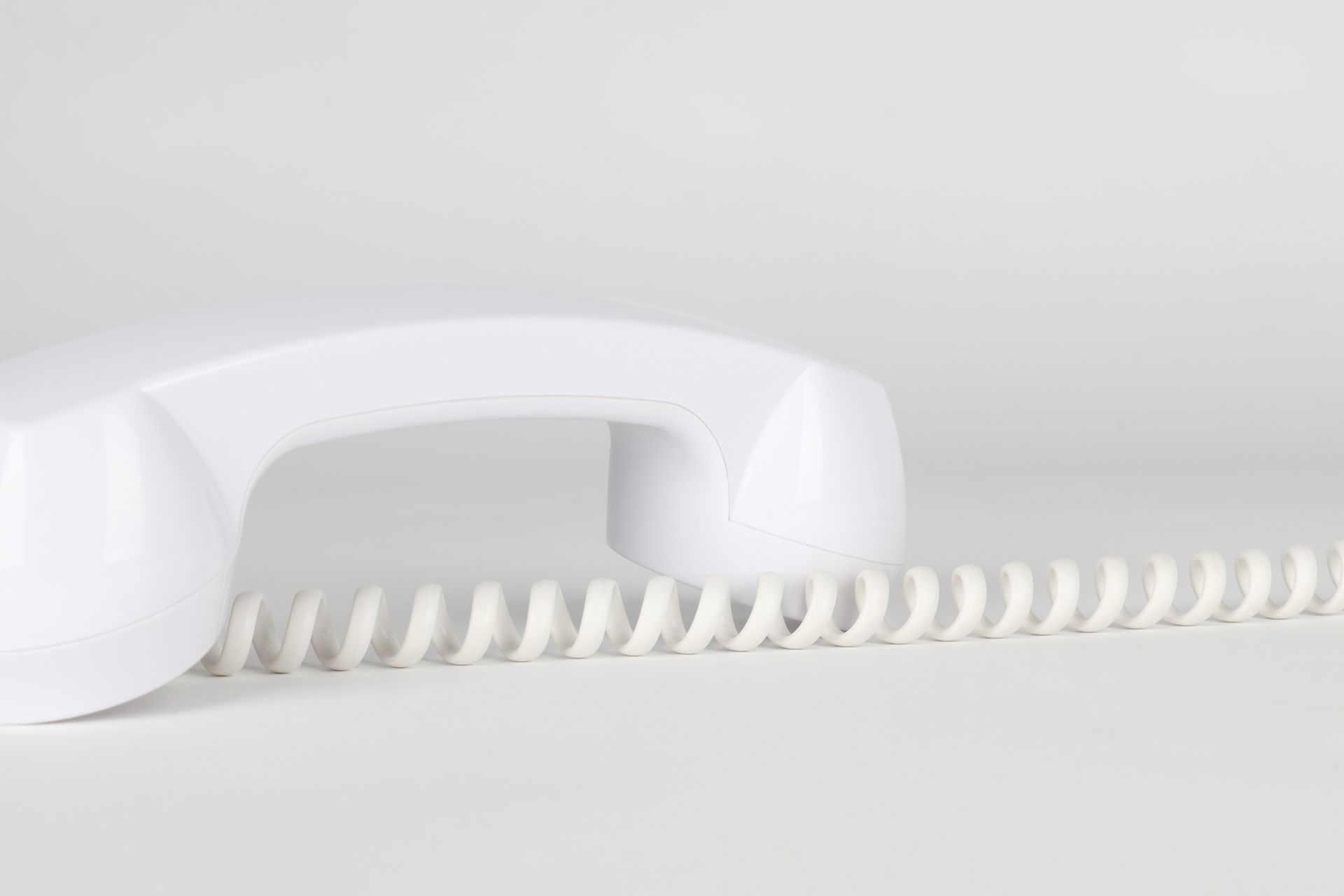 Close-up of a white telephone handset with coiled cord on a neutral background.